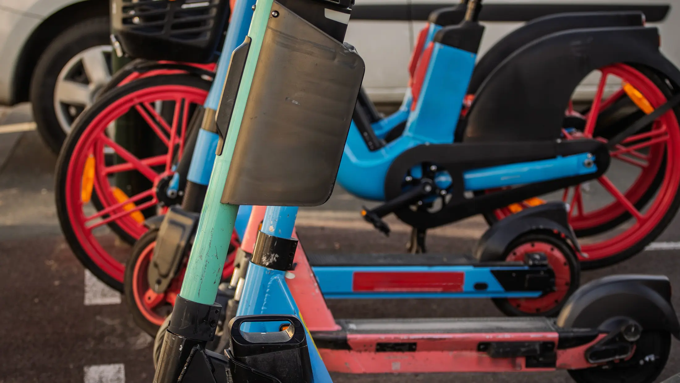 Abgestellte E-Scooter und E-Bikes am Fahrbahnrand neben einem geparkten Auto